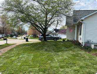 Freshly laid sod on a suburban front lawn, bordered by a driveway and white house. A flag hangs near the house.