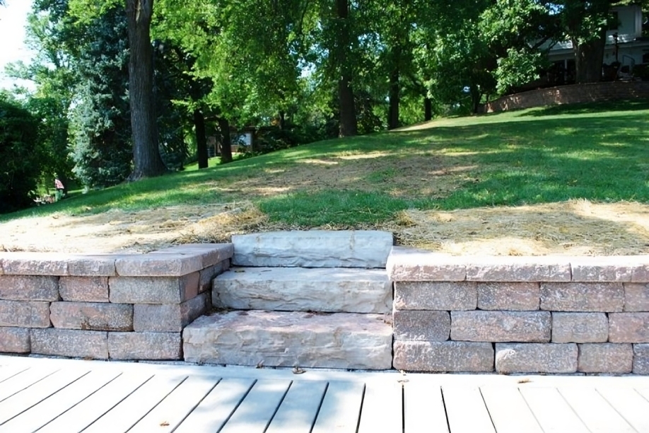 Stone steps leading up to a grassy hill, surrounded by lush green trees. The scene is serene, conveying a peaceful outdoor ambiance.